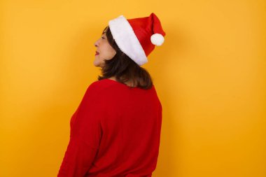 Orta yaşlı Arap bir kadının Noel şapkası takıp duvarın karşısına dikilmesinin arka görüntüsü. Stüdyo Çekimi.