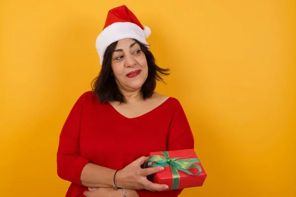 Verträumte Arabische Frau Mittleren Alters Trägt Weihnachtsmütze Mit Geschenk Mit — Stockfoto