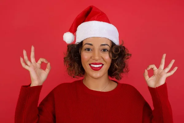 Froh Attraktive Frau Mit Weihnachtsmütze Und Rotem Pullover Zeigt Zeichen — Stockfoto