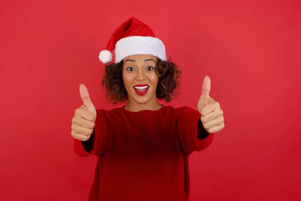 一个戴着圣诞礼帽 头戴红色毛衣 高高兴兴地笑着站在室内的年轻成功女人的画像 — 图库照片
