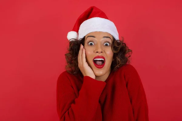 令人惊讶的是 戴着圣诞帽和红色毛衣的女人满脸惊讶地张大了嘴 满脸惊讶 正面情绪面部表情肢体语言 — 图库照片