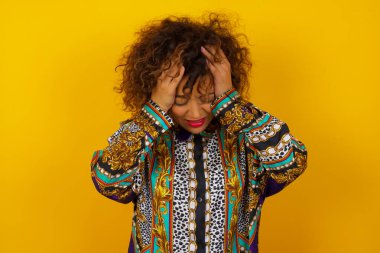 Renkli gömlek giyen genç bir Arap kadın başını izole edilmiş arka planda tutarak acı ve migrenden dolayı çaresiz ve stresli bir baş ağrısı çekiyor. Ellerini başının üstüne koy..