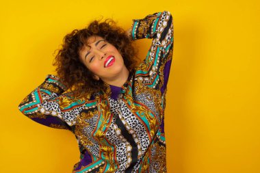 Güven ve cinsel ilişki konsepti. Renkli tişört giyen Arap kadının portresi. Kendine güvenen bir ifadeyle gülümseyen ve ellerini başının üstüne koyan. Arkaplanda duruyor.