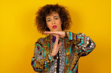 Renkli tişört giyen genç, güzel bir Arap kadın yorgun ve sıkkın, mola jesti yapıyor, iş stresi, zaman kavramı yüzünden durmak zorunda. Duvara yaslanarak.