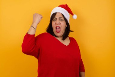 Mutlu, mutlu, mutlu, orta yaşlı, Noel şapkası takan orta yaşlı bir kadın. İyi haberler almaktan memnun, mutluluktan hareketler yapıyor, yumruğunu sıkıyor ve kazanan bir jest yapıyor.. 