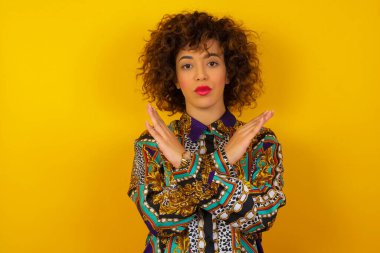 Renkli gömlek giyen, sıradan kıyafetler giyen, izole edilmiş arka planda duran genç, güzel bir Arap kadın. Reddedilme ifadesi olumsuz işaret göndererek el ele tutuşuyor mu?.