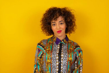 Güzel bir Arap kadının renkli gömlekli, kıvırcık saçlı, sevimli bir gülümsemeyle kameraya bakarken içeriğiniz için beyaz, boş bir fotokopi duvarına poz verirken yakın çekimini yapın.