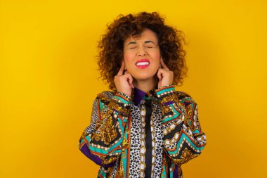 Bu sinir bozucu sesi çıkarmayı kes! Mutsuz, renkli gömlek giyen, endişeli yüz ifadeleri takınan, parmaklarıyla kulakları tıkayan, üst katındaki komşulardan gelen gürültüden rahatsız olan Arap kadını strese sokuyor..