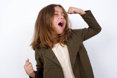 Beyaz arka plan karşısında duran çekici küçük kız zaferi kutluyor yumruklarıyla havaya yumruk atıyor ve beyaz bir stüdyonun arka planında sahte uzay ile ışıldayan dişli bir gülümseme..