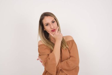 Düşünceli gülümseyen bir kadının portresi elini çenesinin altında tutar, doğrudan kameraya bakar, ilgiyle karışık bir şey dinler, sıradan giyinir, beyaz duvara karşı poz verir..