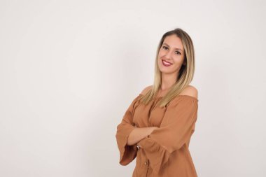 Kolları çapraz beyaz, beyaz duvara yaslanmış, sıradan kıyafetler giyen beyaz bir kadın. Kameraya bakıp gülümsüyor. Kendine güvenen başarılı bir kadın..