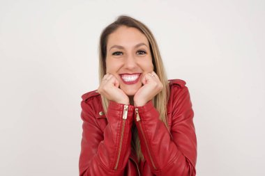 Hayalperest genç Avrupalı kadın ellerini çenesinin altına bastırıyor, mutlu bir ifadeyle bakıyor, dişlek gülüşü var, gri arka planda soyutlanmış.