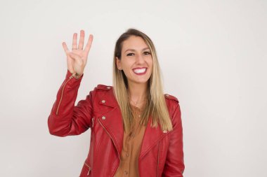 Gri duvara yaslanmış genç bir kadın gülümseyerek kendinden emin ve mutlu bir şekilde dört numarayı işaret ediyor..