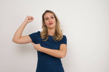 Güzel, beyaz, sarışın, mavi elbiseli, kolunu gösteren bir kadın. Beyaz arka planda duruyor. Reklam kavramı. 