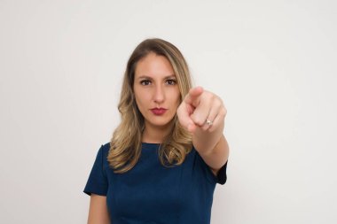 Mavi elbiseli, güzel, beyaz, sarışın kadın seni işaret ediyor. Stüdyonun arka planında duruyor. Reklam kavramı.