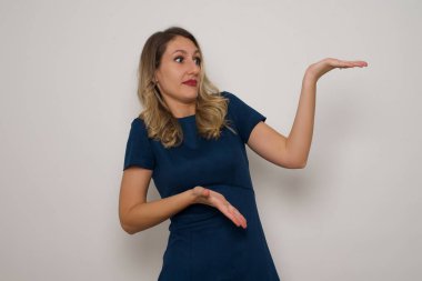 Güzel, beyaz, şaşırmış kadın bir şey gösteriyor. Gri arka planda duruyor. Reklam kavramı.