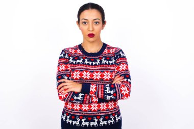 Kızgın, genç, güzel bir Arap kadının Noel süveterini beyaz duvara dayadığı bir fotoğraf..