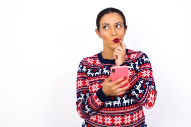 Genç ve güzel bir Arap kadının Noel süveteri giydiğini cep telefonu kullandığını ve el ele tutuştuğunu hayal etmek. Karar almak ve sosyal medya kavramı.