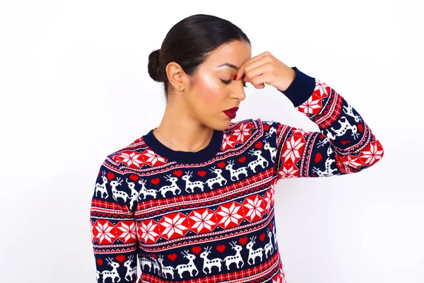 白い壁にクリスマスのセーターを身に着けている非常に動揺した 若い美しい女性は 目を閉じた間の鼻に触れ 泣きたい ストレスの多い関係を持っている または仕事に問題を抱えている — ストック写真