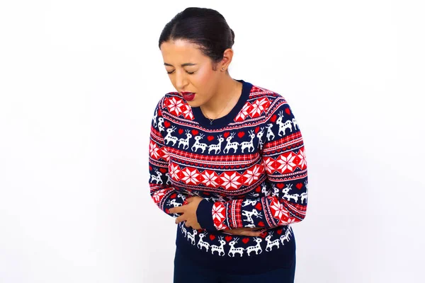 強い胃袋に苦しむ白い壁に対してクリスマスのセーターを身に着けている若い美しい女性 — ストック写真