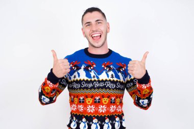 İyimser beyaz adam beyaz duvara karşı Noel süveteri giyip olumlu duygular besliyor. Kalite ve tavsiye kavramı.