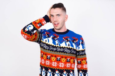 Kafası karışmış beyaz bir adamın portresi Noel süveteri giymiş beyaz bir duvara yaslanmış saçların üstünde el ele tutuşmuş, kaşlarını çatmış, paniklemiş, hafızasını kaybetmiş. Endişeli ve endişeli. Hiçbir şey hatırlayamıyor..