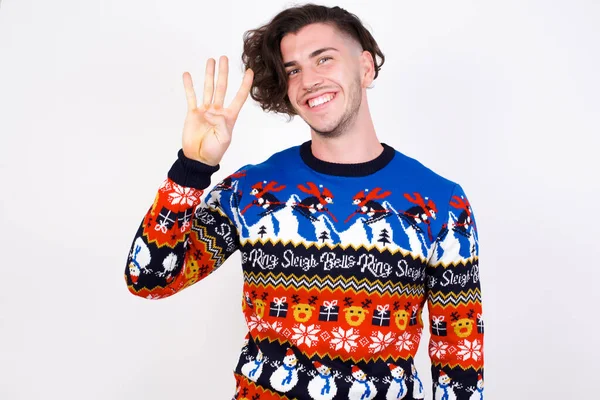 若い白人男性はセーターを着て 自信を持って幸せに微笑んでいる間 指番号4を指で指で指を指さす — ストック写真