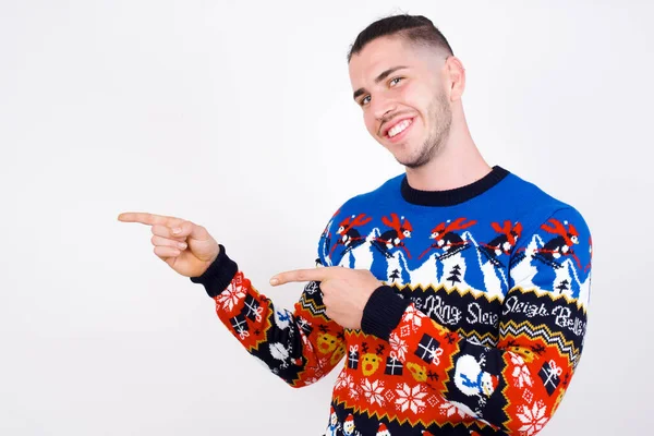 Kaukasische Man Draagt Kerst Trui Tegen Witte Muur Punten Opzij — Stockfoto