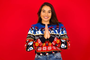 Kızıl duvara karşı Noel süveteri giyen, avuçlarını bir arada tutan, mutlu bir yüzü olan güzel beyaz kadın. Çekici bir erkek merhamet diliyor. Umutlu genç yetişkin.