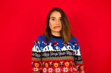 Kızıl duvara karşı Noel süveteri giyen genç, beyaz bir kadın gergin ve korkmuş dudakları ısıran, sabırsız ifadeli kameraya bakan, düşünceli..