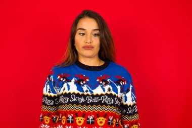 Genç, güzel, beyaz bir kadın Noel süveterini kırmızı duvara dayamış, şaşı gözlü, dudaklarını buruşturan, garip ifadeyle yüzünü buruşturan yalnız başına eğleniyor, aptal rolü yapıyor..