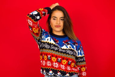 Genç, güzel, beyaz bir kadın Noel süveterini kırmızı duvara dayayıp 