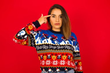 Mutsuz Kafkasyalı kadın Noel süveterini kırmızı duvara dayayıp dudaklarını kıvırıyor ve intihar jesti yapıyor, eliyle şakağına ateş ediyor, kendini öldürmeye çalışıyor..