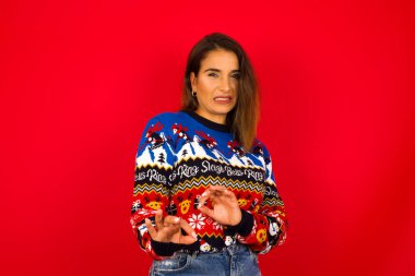 Ne kadar iğrenç! Kızıl duvara karşı Noel süveteri giyen beyaz kadın, iğrenç bir şey gördüğü için tatminsiz bir yüz ifadesi sergiliyor..