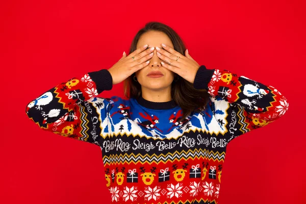 Genç, beyaz bir kadın, kırmızı duvara karşı Noel süveteri giyiyor, iki eliyle gözlerini kapatıyor, hiçbir şey görmek ya da utanmak istemiyor. İnsani duygular tepki verir.