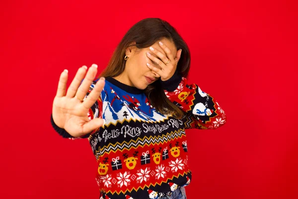 Kaukasische Frau Trägt Weihnachtspullover Vor Roter Wand Bedeckt Augen Mit — Stockfoto