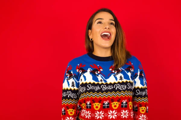 Mujer Caucásica Sorprendida Vistiendo Suéter Navidad Contra Pared Roja Encoge —  Fotos de Stock