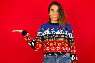 Kırmızı duvara karşı Noel süveteri giyen genç, güzel beyaz bir kadın, 