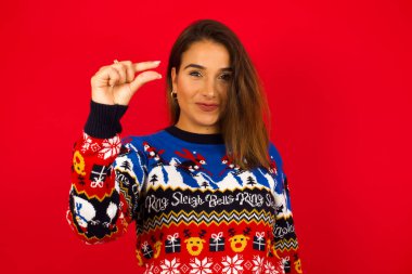 Kırmızıya dayalı Noel süveteri giyen genç, beyaz bir kadın, küçük bir el hareketini çok küçük bir boyutta gösteriyor. Çok fazla değil.