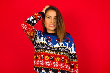 Kafası karışmış genç beyaz bir kadının portresi. Kırmızı duvara karşı Noel süveteri giymiş, saçlarına el ele tutuşmuş, kaşlarını çatmış, paniklemiş, hafızasını kaybetmiş. Endişeli ve endişeli. Hiçbir şey hatırlayamıyor..