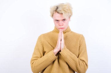 Beyaz arka plana karşı duran yakışıklı, beyaz tenli sarışın adam avuçlarını önünde birbirine bastırıyor. Pişman görünüyor, af diliyor. Lütfen beni affet..