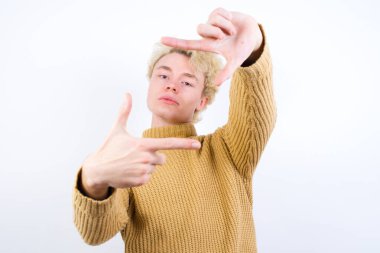 Pozitif yakışıklı, beyaz arka planda duran beyaz saçlı, neşeli bir adam, iyi bir ruh hali var, kameraya doğru hareketli bir parmak çerçevesi var..