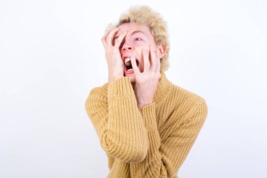 Genç, kasvetli, beyaz arka plan karşısında duran, elleri somurtkan, ağlayan, üzgün ve depresif bir şekilde duran, iş probleminden şikayet eden kasvetli, beyaz saçlı, sarışın bir adam..