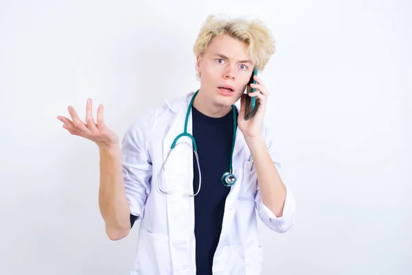 Joven Médico Rubio Bata Blanca Estetoscopio Hablando Por Teléfono Estresado —  Fotos de Stock
