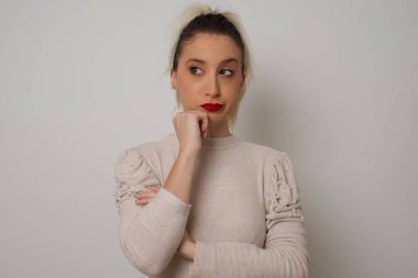 Düşünceli kadın portresi elini çenesinin altında tutuyor, bir şey hatırlamaya çalışıyor ya da ilgi çekici bir şey dinliyor, sıradan giyiniyor, içeride poz veriyor. Gençlik kavramı.