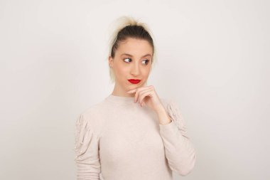 Hoş bir yüzü olan, günlük giysiler giyen, yan bakan, elini çenesinin altında tutan, hoş bir şeyler düşünen, gri arka planda poz veren hayalperest bir kadın..