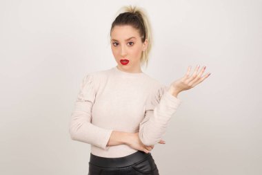What the hell are you talking about, nonsense. Studio shot of frustrated female with blonde hair gesturing with raised palm, frowning, being displeased and confused with dumb question over gray wall.