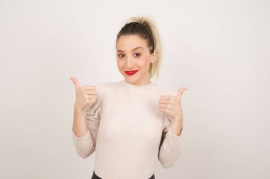 Gri arka planda izole edilmiş, olumlu içerik ve mutluluk duygularıyla baş parmaklarını gösteren iyimser genç bayana yakın çekim. Ortak alan, kalite ve tavsiye ile tatmin kavramı.