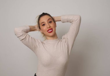 Güven ve cinsel ilişki konsepti. Çekici genç iş kızı portresi, kendine güvenen bir ifadeyle gülümseyen ve ellerini başının üstünde tutan. Arkaplanda duruyor.