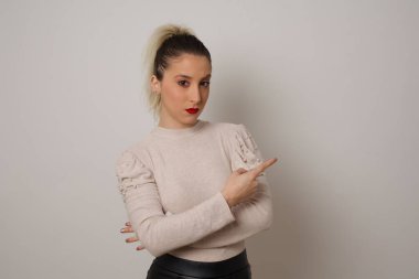 Moda reklamcılığı ve tanıtım metniniz için gri arka planınızın fotokopisini çeken heyecanlı, modacı kız mutlu bir şekilde işaret ediyor..